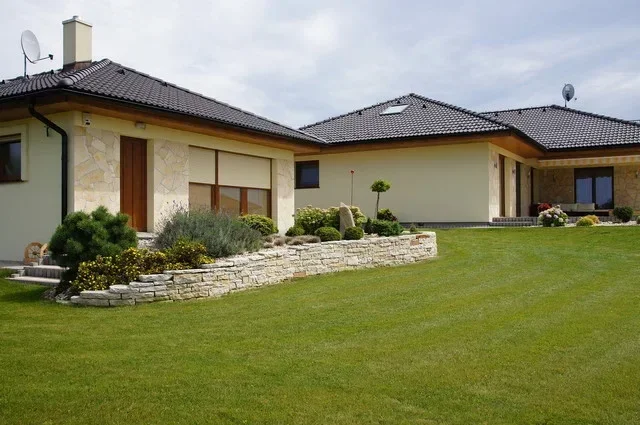 Rodinný dům IRIDA z boku, kamenná opěrná zeď a sečený trávník