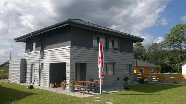 Dokončený dvoupodlažní dům v šedé fasádě s terasou, slunečníkem a trávníkem