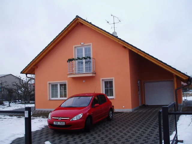 Oranžová fasáda domu VERONIKA s garáží, červený automobil na vjezdu