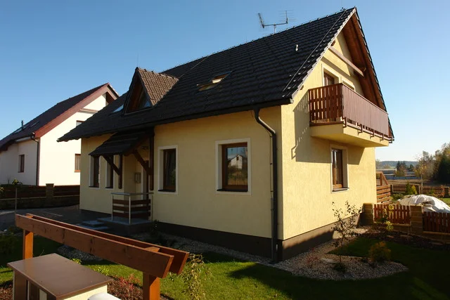 Dům APOLLON s dřevěným balkonem a vstupní stříškou v podzimní zahradě