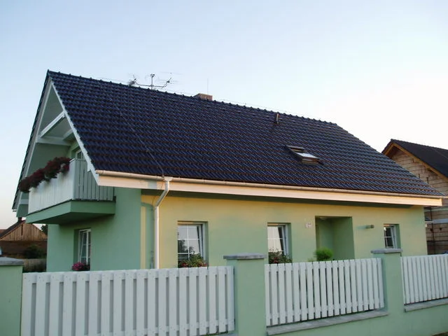 Dům APOLLON za soumraku s bílým laťkovým plotem a balkonem