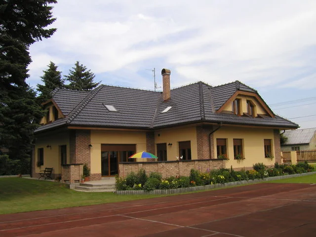 Dům FORTUNA se žlutou fasádou, cihlovými detaily a terasou se slunečníkem
