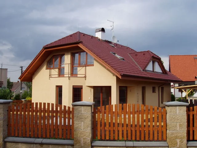 Realizovaný dům HERA s balkonem a prosklením ve štítu za dřevěným plotem