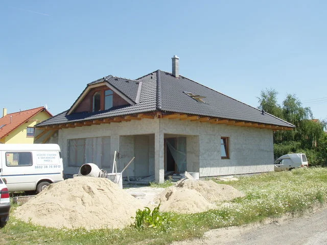 Dům Charis s dokončenou tmavou střechou, hromady písku před stavbou