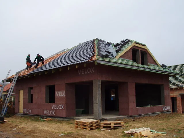 Pokrývači kladou tašky na střechu rozestavěného domu Charis se stěnami VELOX