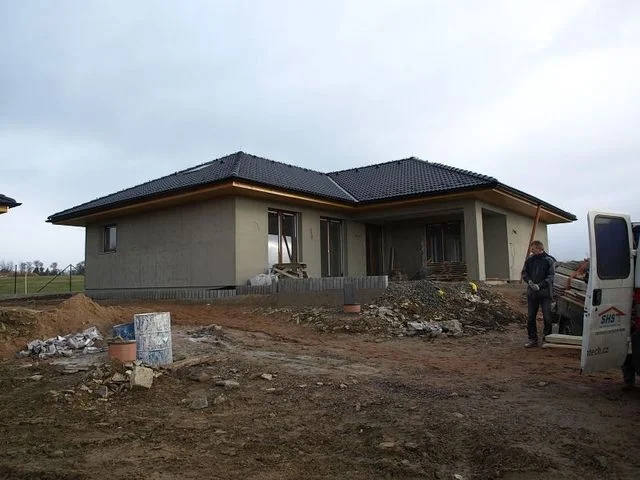 Dům Irida ve fázi podkladních omítek, neupravený terén a dodávka na stavbě