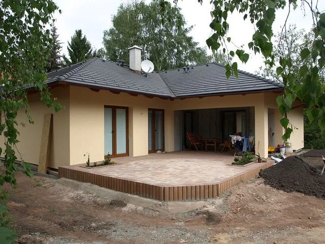 Realizovaný dům Irida se žlutou fasádou a dlážděnou terasou v zahradě