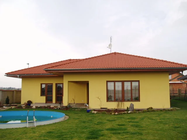 Žlutý bungalov IRIS s červenou valbovou střechou a bazénem na zahradě