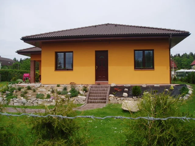 Vstupní průčelí oranžového bungalovu IRIS s betonovými schody a skalkou