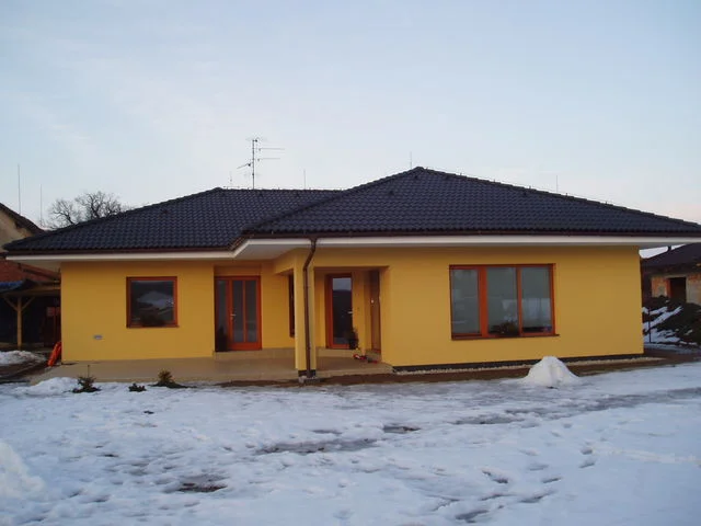 Zimní čelní pohled na žlutý bungalov IRIS se zasněženou zahradou