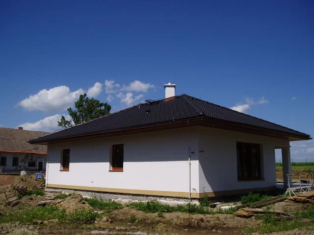 Rozestavěný bungalov IRIS s hotovou střechou a bílou omítkou, neupravené okolí