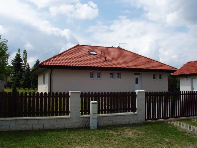 Bungalov IRIS s červenou taškovou střechou za tmavým dřevěným plotem