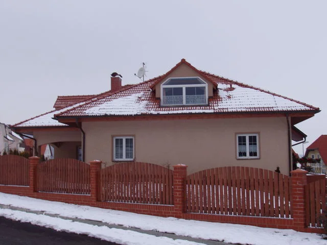 Zasněžený dům AFRODITE s béžovou fasádou a cihlovým plotem v zimě