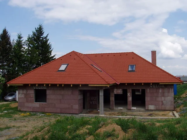 Rozestavěný dům AFRODITE s hotovou červenou střechou a neomítnutým zdivem VELOX