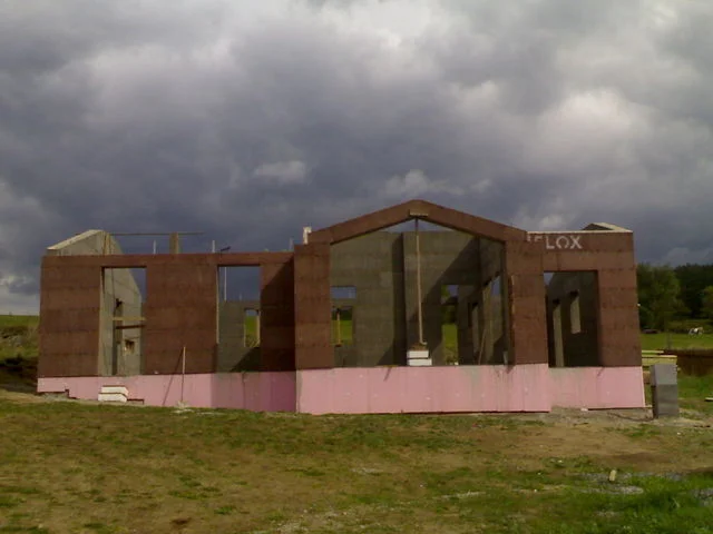 Stavba domu MINERVA II z VELOXu s růžovou izolací soklu pod zataženou oblohou
