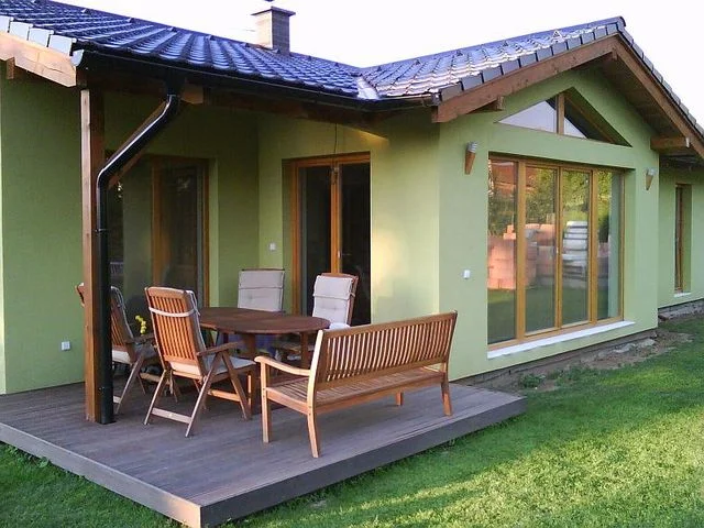 Krytá dřevěná terasa se zahradním nábytkem u zelené fasády domu Minerva II
