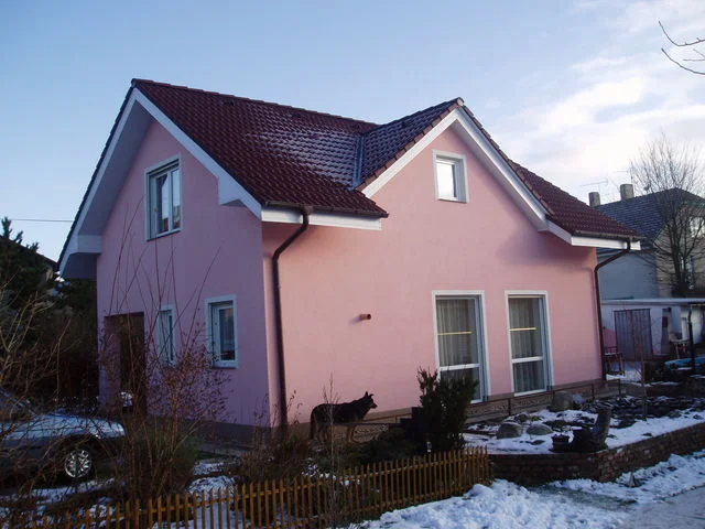 Dokončený dům Mini s růžovou fasádou a sedlovou střechou, zasněžená zahrada