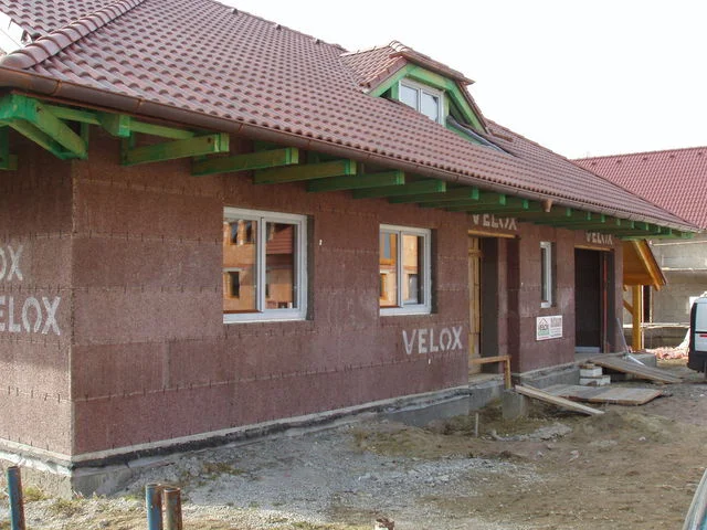 Detail hrubé stavby NIKÉ se zabudovanými okny a zelenou dřevěnou konstrukcí přesahu