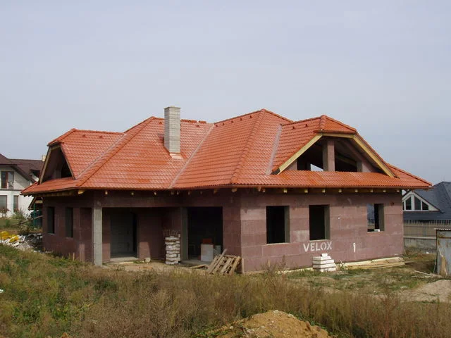 Hrubá stavba NIKÉ s oranžovou valbovou střechou při pohledu z pozemku