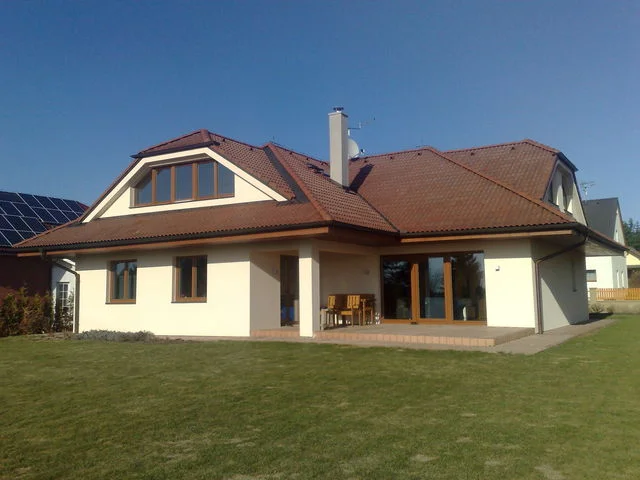 Dokončený dům NIKÉ s bílou fasádou, cihlovou valbovou střechou a travnatou zahradou