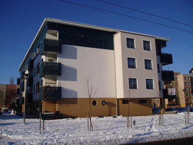 Bytový dům s prosklenými balkony, v pozadí panelový dům, zimní den