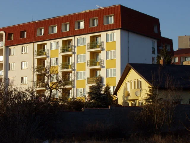 Boční pohled na bytový dům Větrník nad žlutým rodinným domem