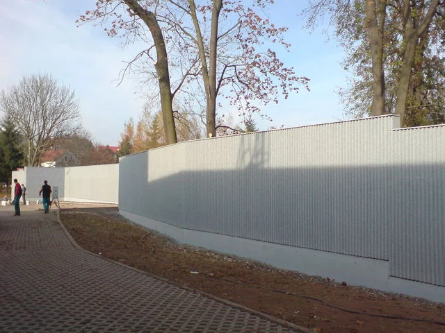 Dokončená světlá protihluková stěna zakřivená podél dlážděné cesty