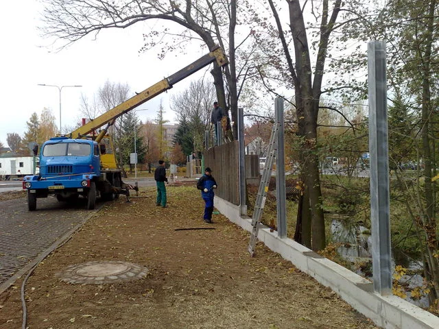 Autojeřáb podává panel pracovníkům při montáži protihlukové stěny