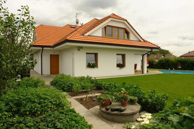 Vstupní strana rodinného domu FORTUNA s oranžovou střechou a osázenou předzahrádkou